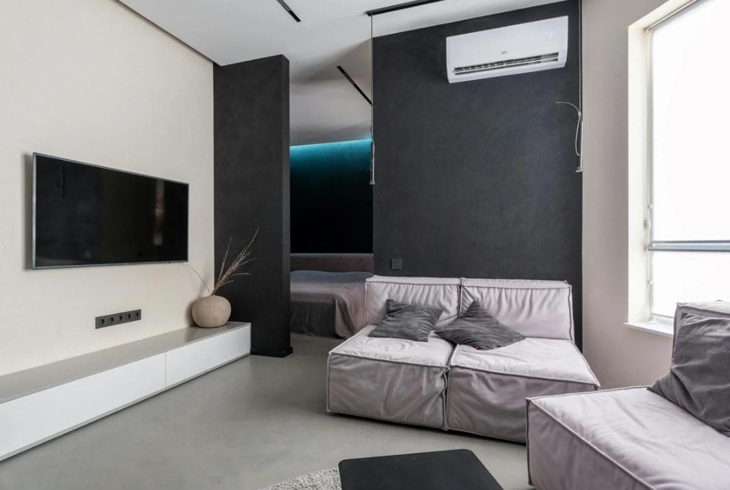 A chic minimalist bedroom with a modular couch, a wall-mounted TV, and a subtle color palette, highlighted by a sleek air conditioner above