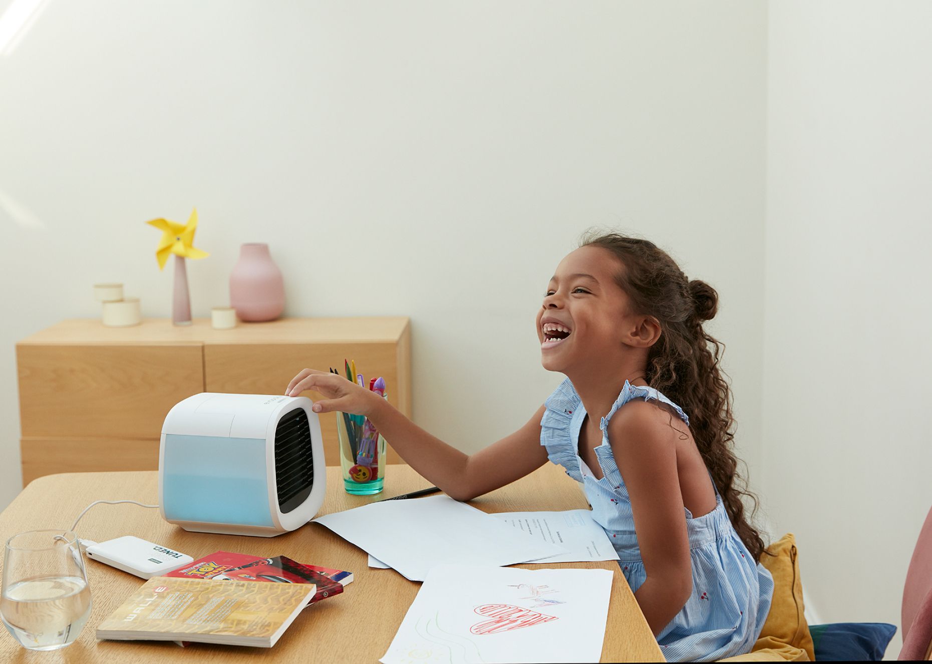 A young girl smiling and touching a portable evapolar air cooler